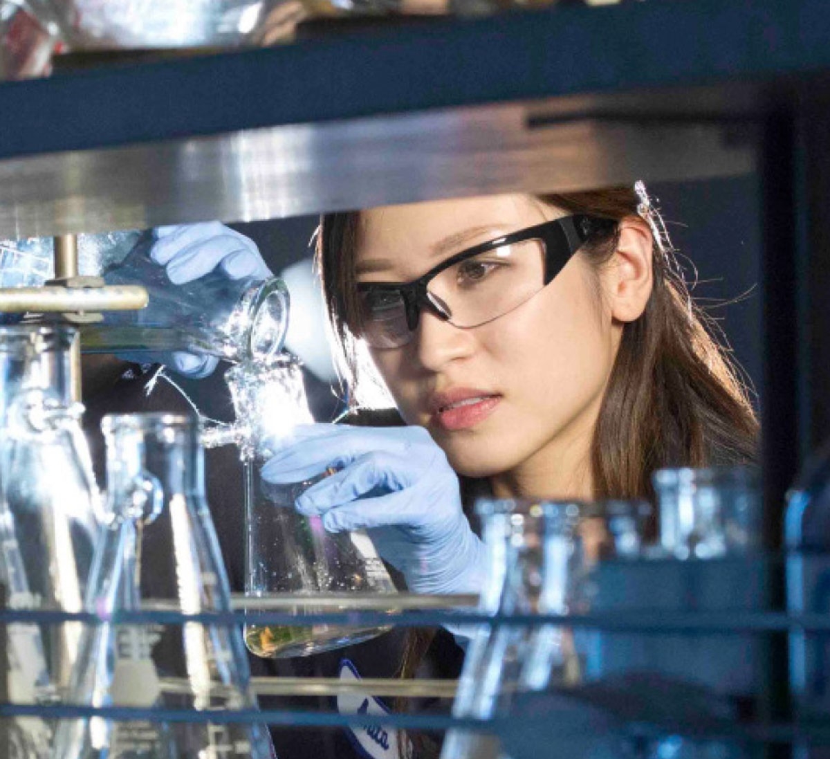 someone in a lab concentrating and pouring liquid into a glass beaker.