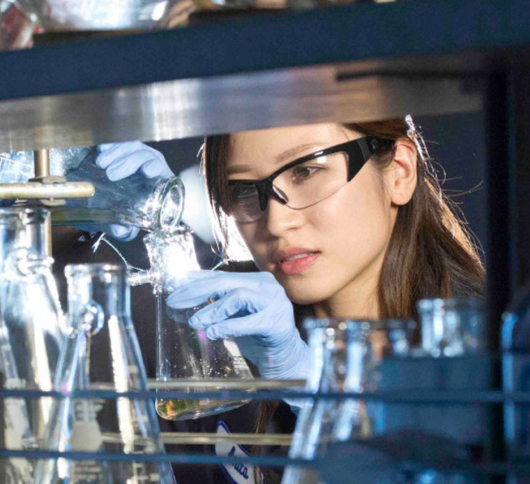 someone in a lab concentrating and pouring liquid into a glass beaker.